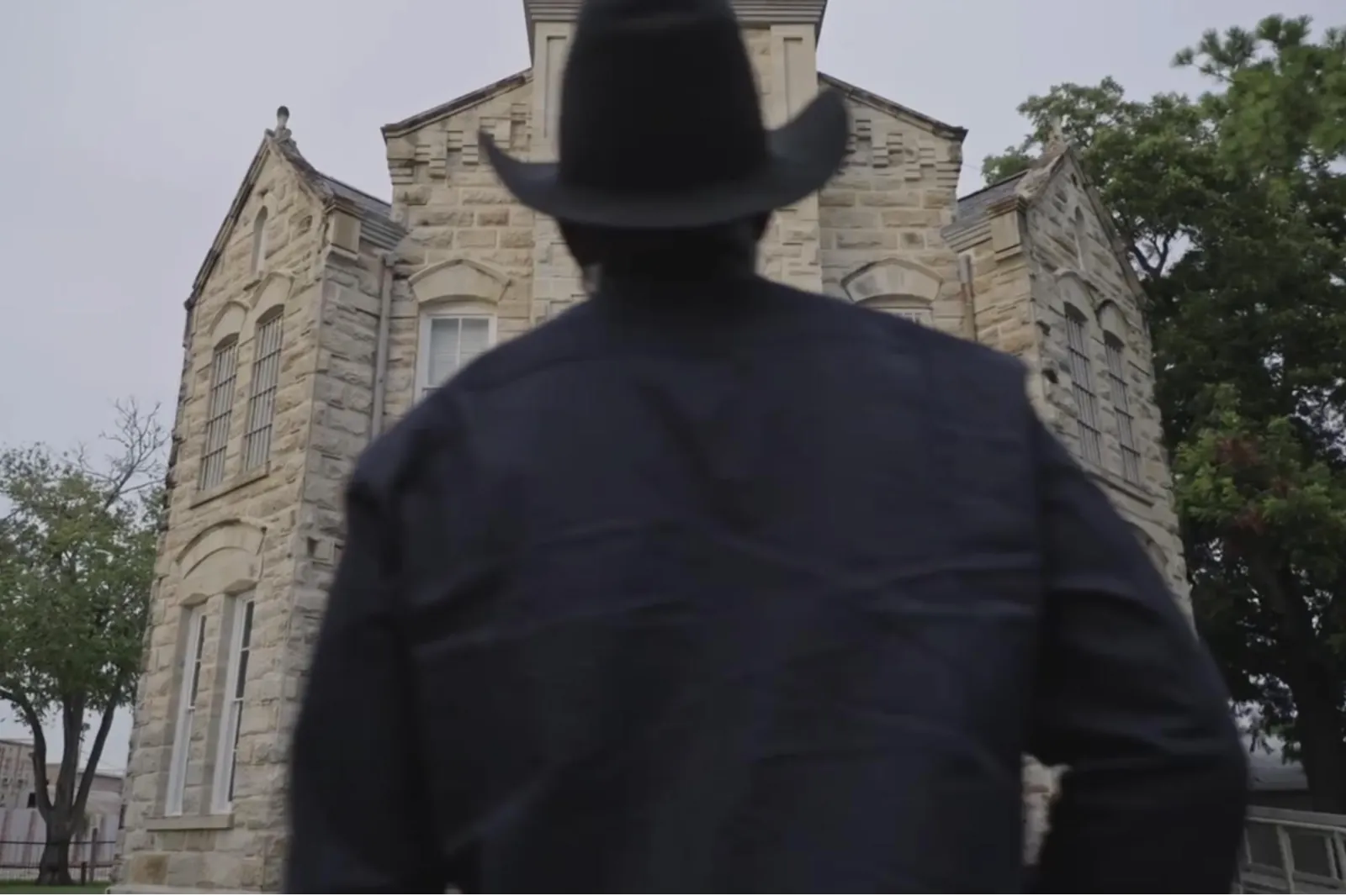 Silhouette of a man in a cowboy hat before a stone building